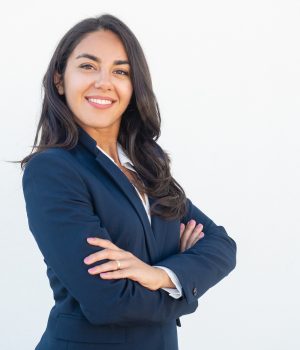 Smiling confident businesswoman posing with arms folded. Happy beautiful black haired young Latin woman in formal suit standing for camera over white studio background. Corporate portrait concept